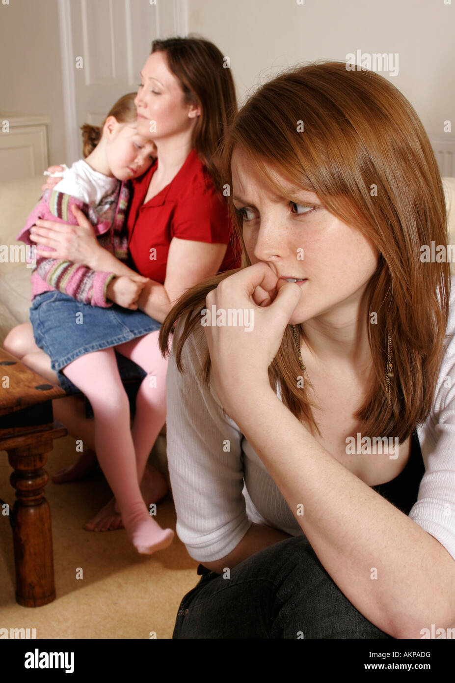 Mother comforting little girl and concerned young woman in foreground Stock Photo