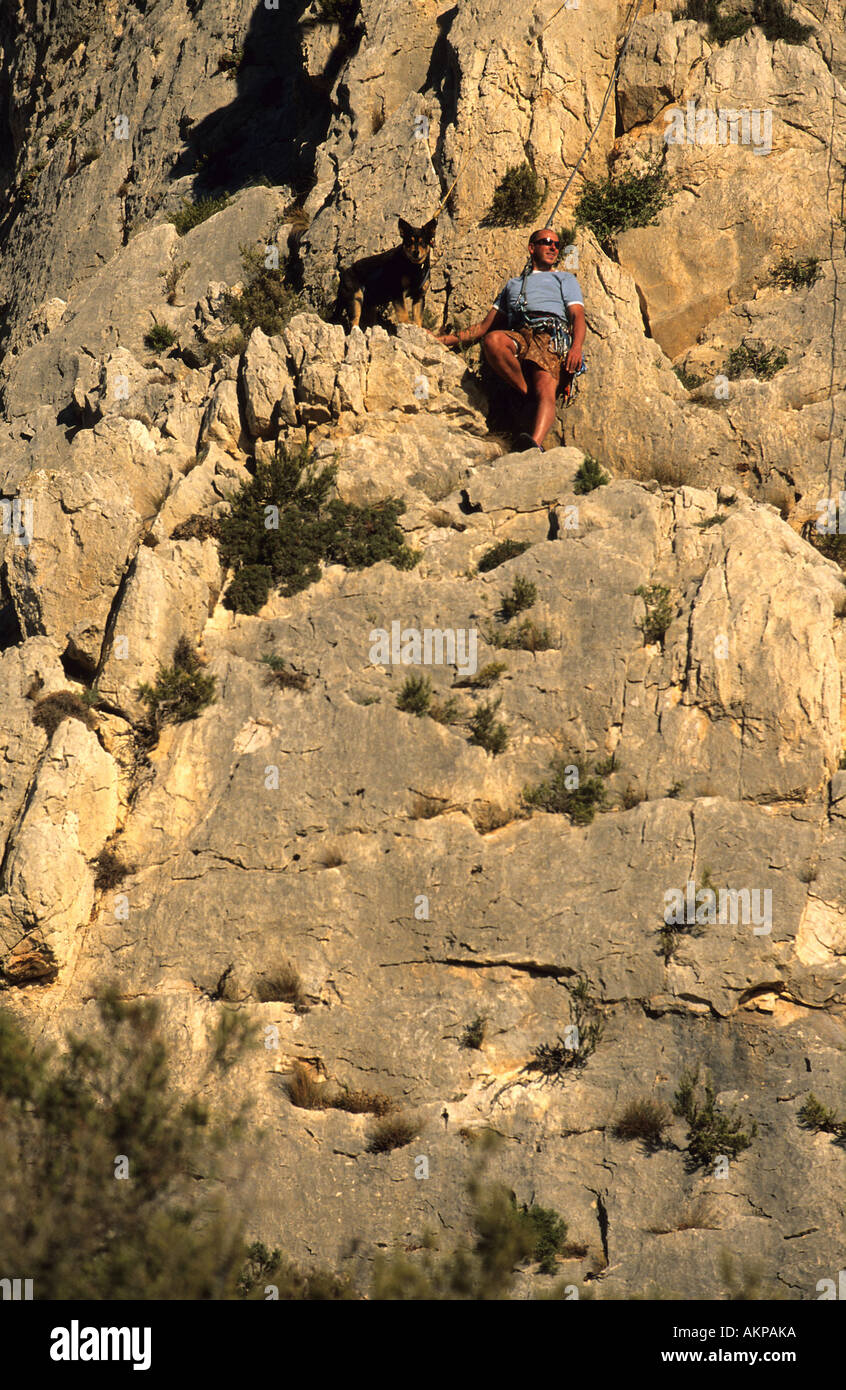 Man crosses a rock face with his dog on ropes Stock Photo