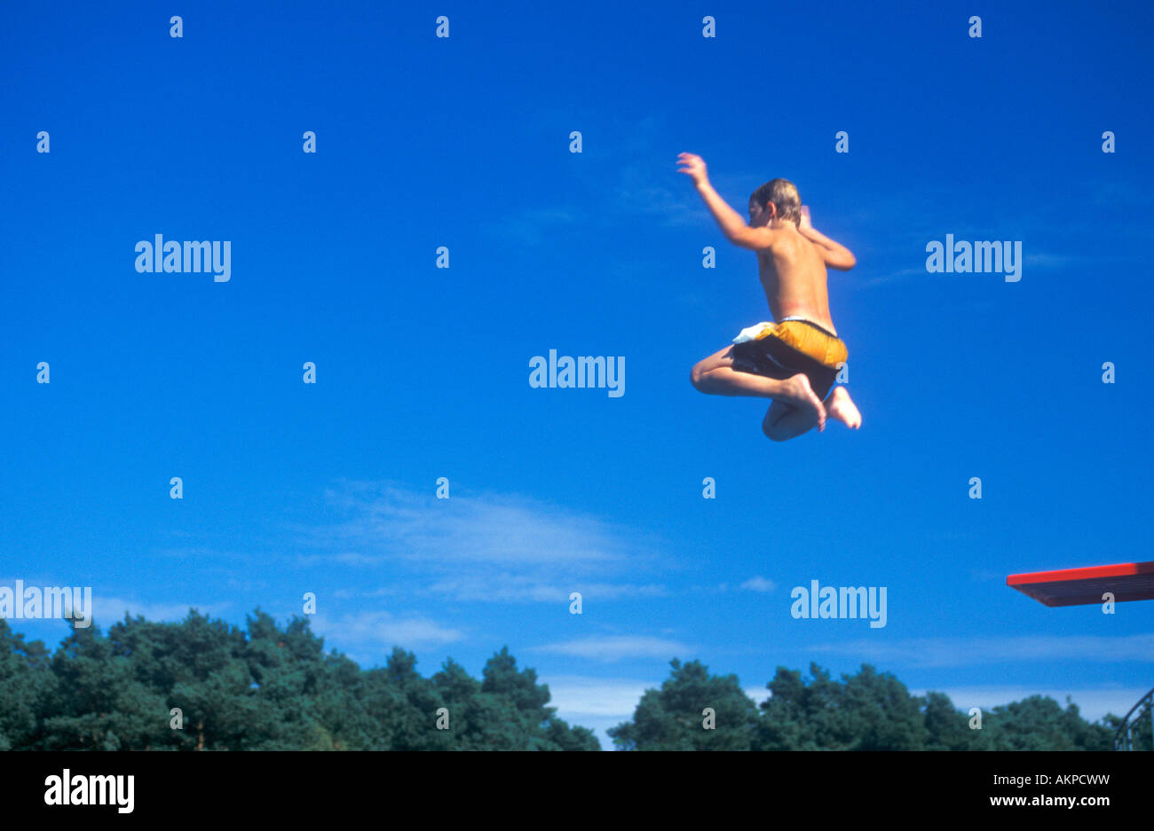 young boy jumping off a diving board at an open air bath Stock Photo