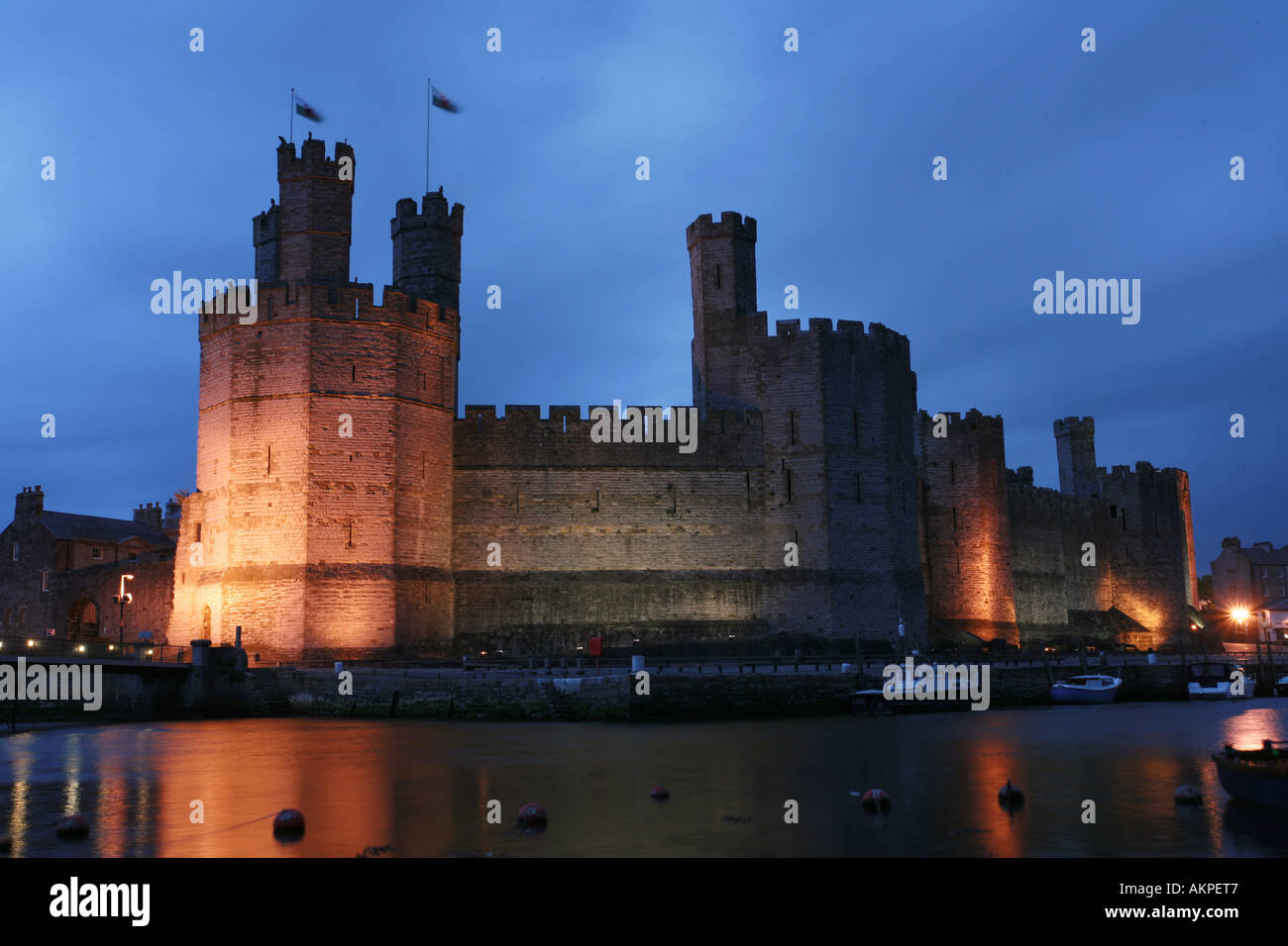 Caernarfon castle bathed in spotlights at dusk with stormy sky