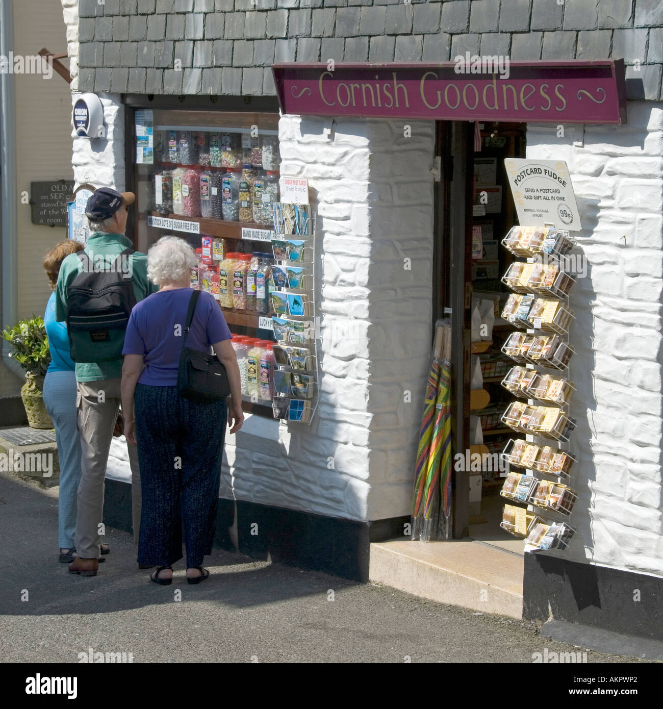 Older tourist couple window shopping & looking at sweet shop named 'Cornish Goodness' in Polperro fishing village in Cornwall West Country England UK Stock Photo