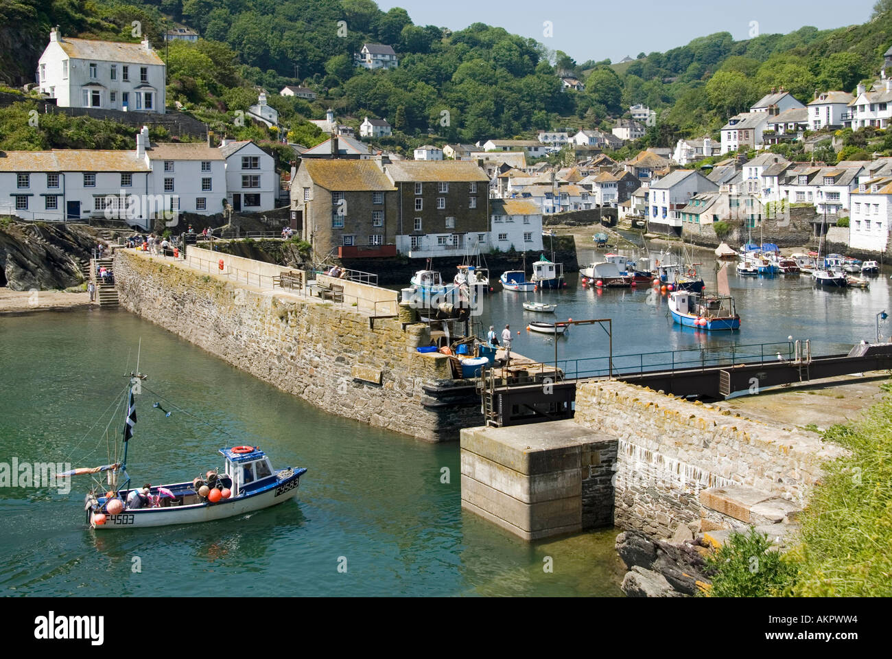 River Pol widens out into Polperro a Cornish coastal village & fishing harbour with wall as boat returns backdrop of B&B cottages Cornwall England UK Stock Photo