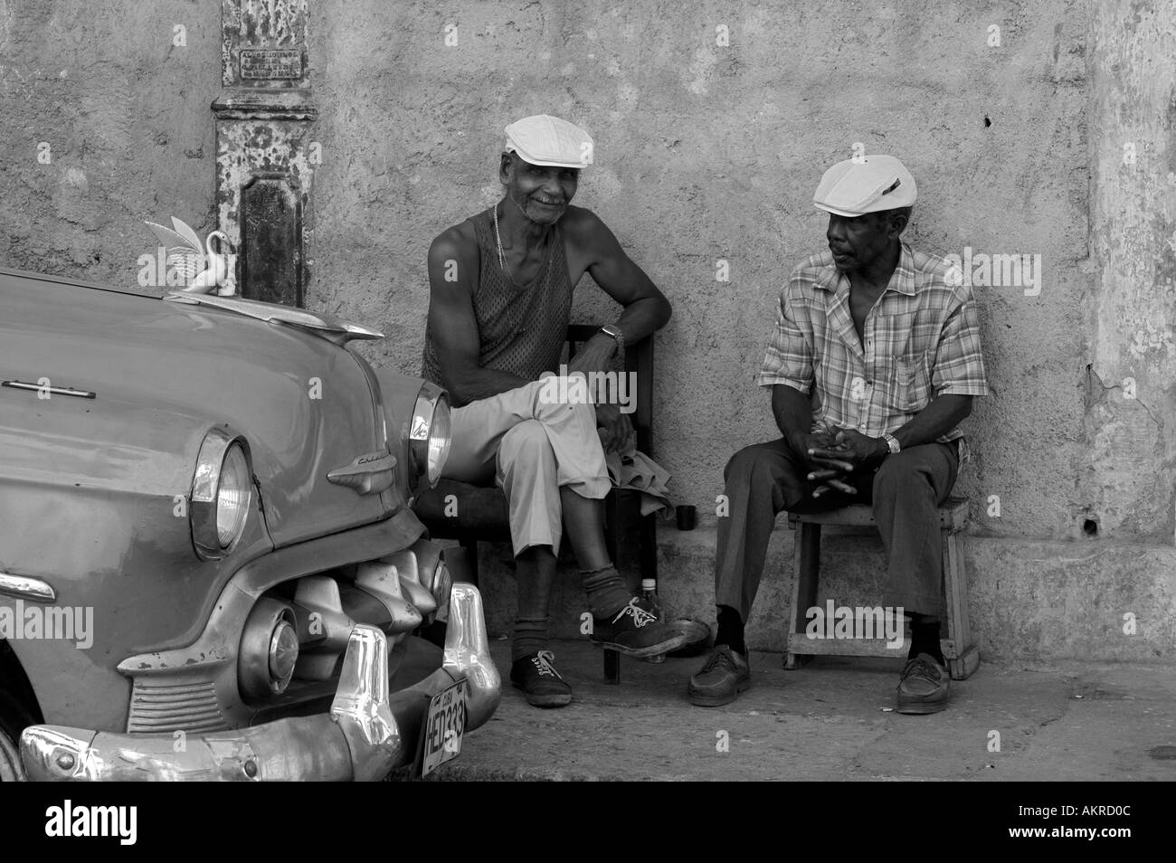 two cuban men sit talking by an old american car Stock Photo