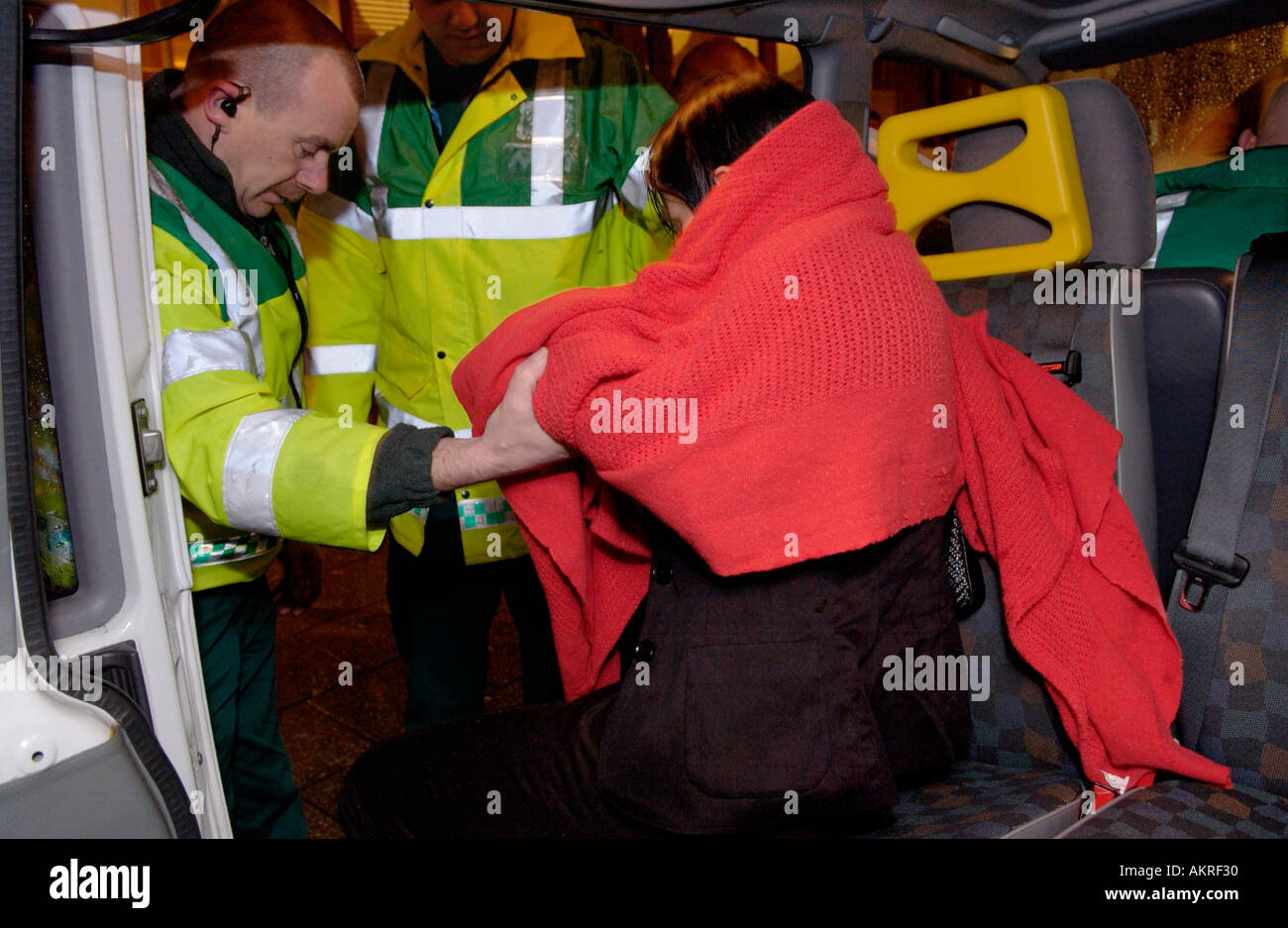 Paramedics helping a young woman wrapped in red blanket into an