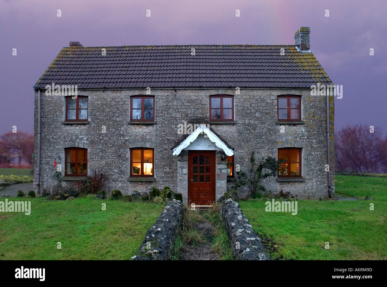 Welsh Farm House with one lit window and a storm and rainbow behind it