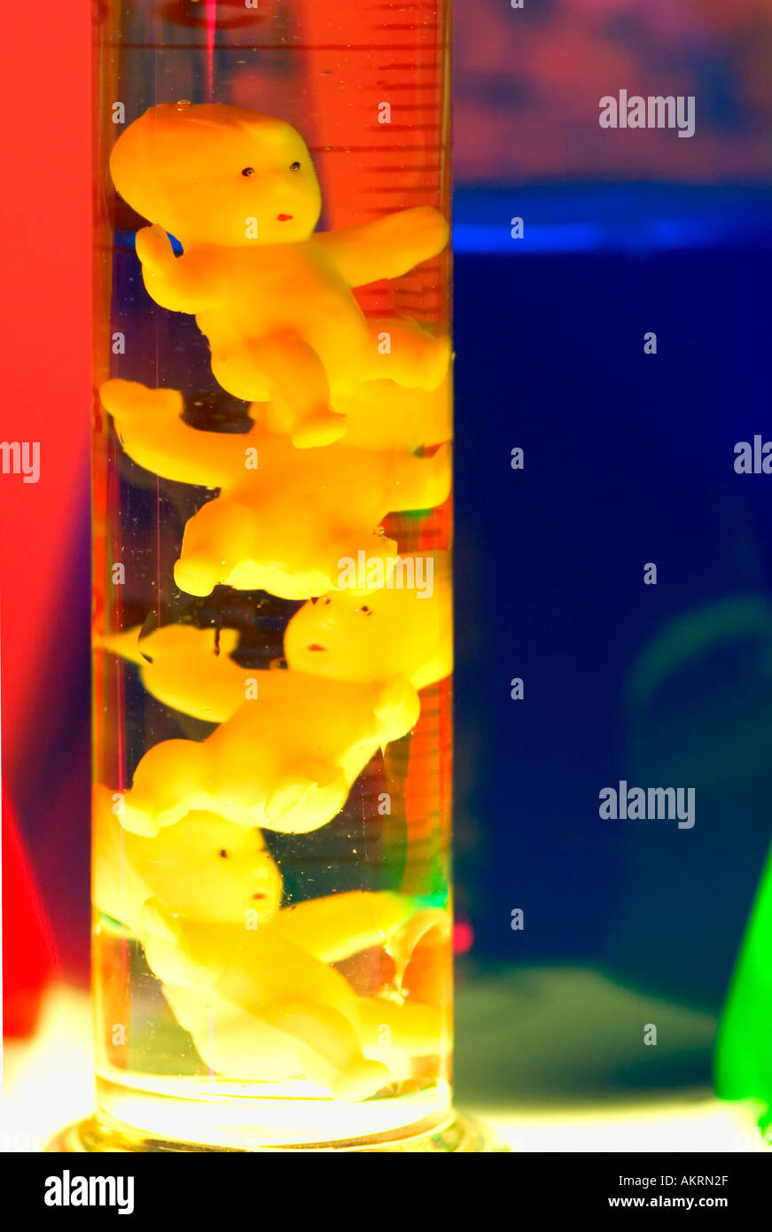 Four plastic baby dolls in a test tube filled with colorful glowing liquid Stock Photo
