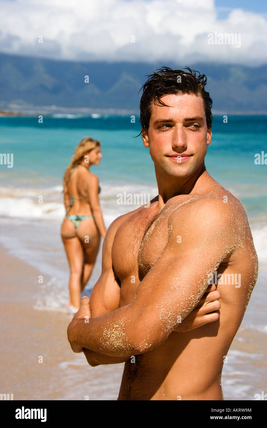 Handsome man standing on Maui Hawaii beach with woman in background Stock Photo
