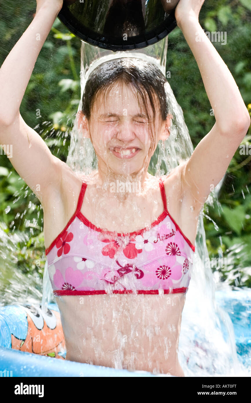 A young girl tipping a bucket of water over her head in a paddling pool