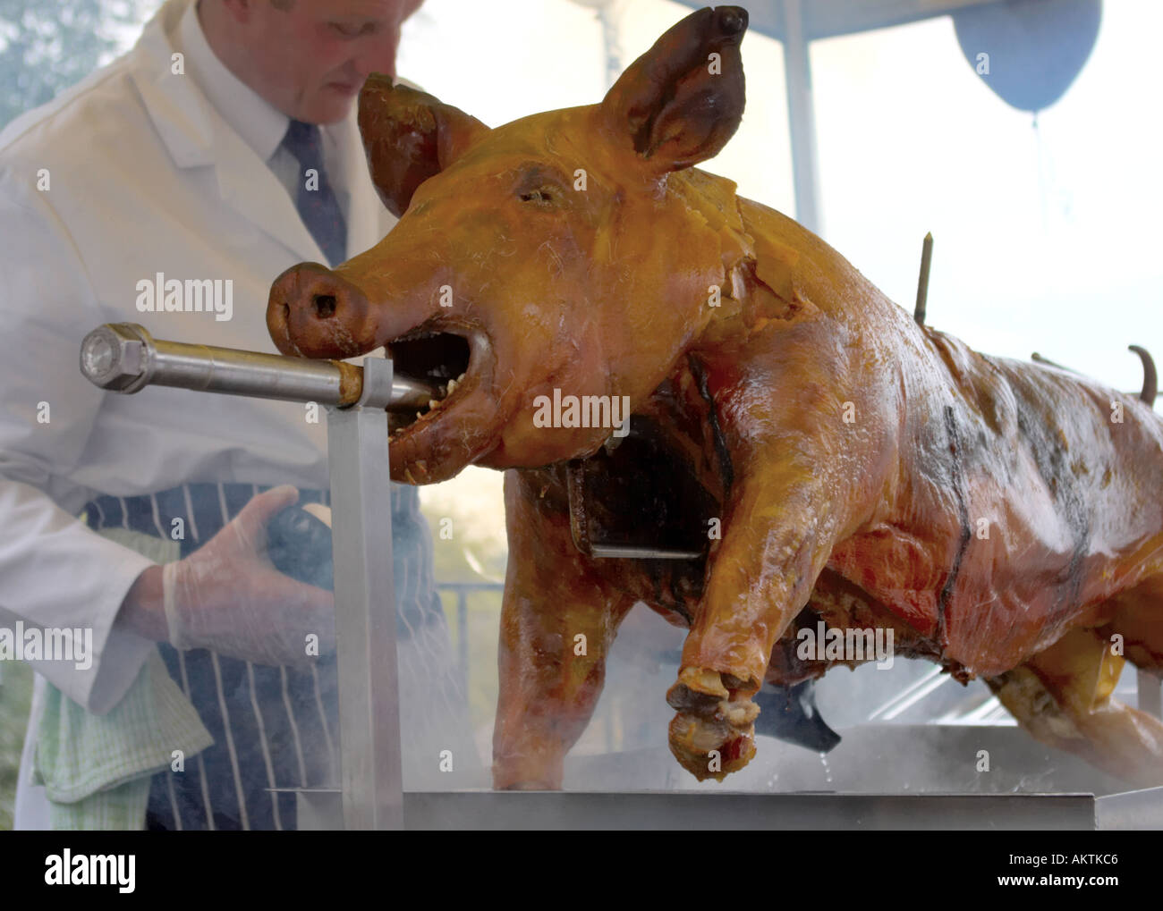 a whole pig roasting on a barbeque spit with cook Stock Photo Alamy