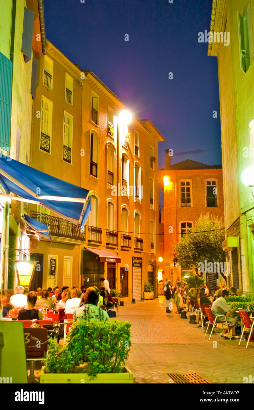 French Restaurant Crowded Terraces, Pedestrian Street Scene Perpignan South of France in Old Town Center, Street Lamps at Night Stock Photo