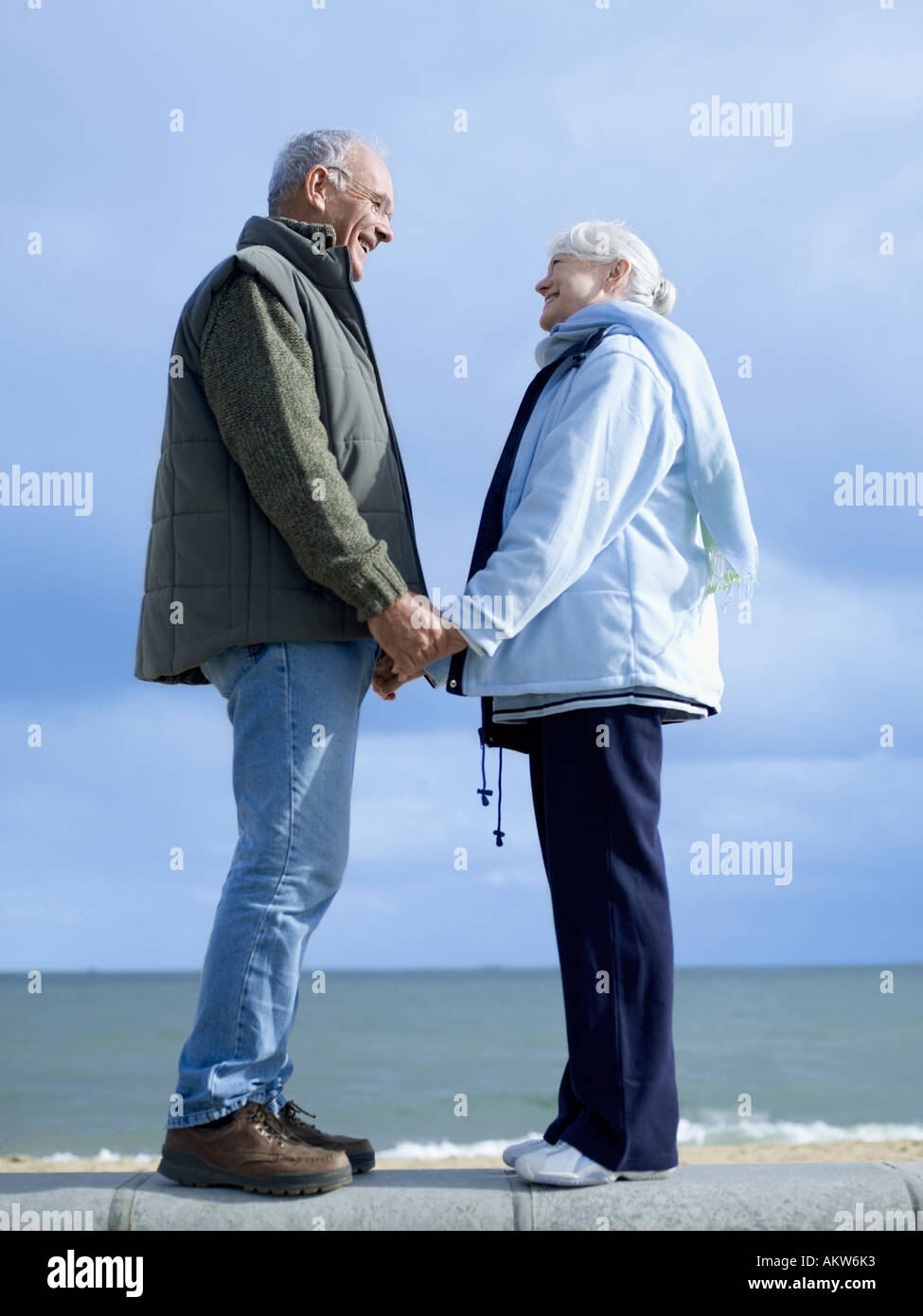 Senior couple standing on wall by water, holding hands Stock Photo