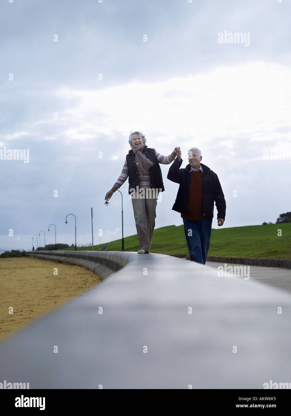 Senior couple walking on wall, holding hands Stock Photo