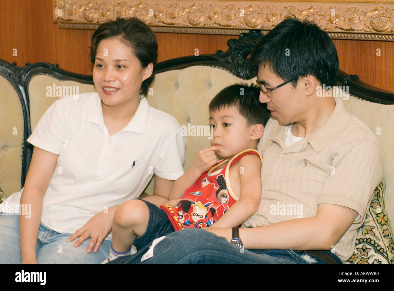 Asian Boy Sitting On Fathers Lap Next To Mother On Sofa Watching TV In Living Room Taiwan China Stock Photo