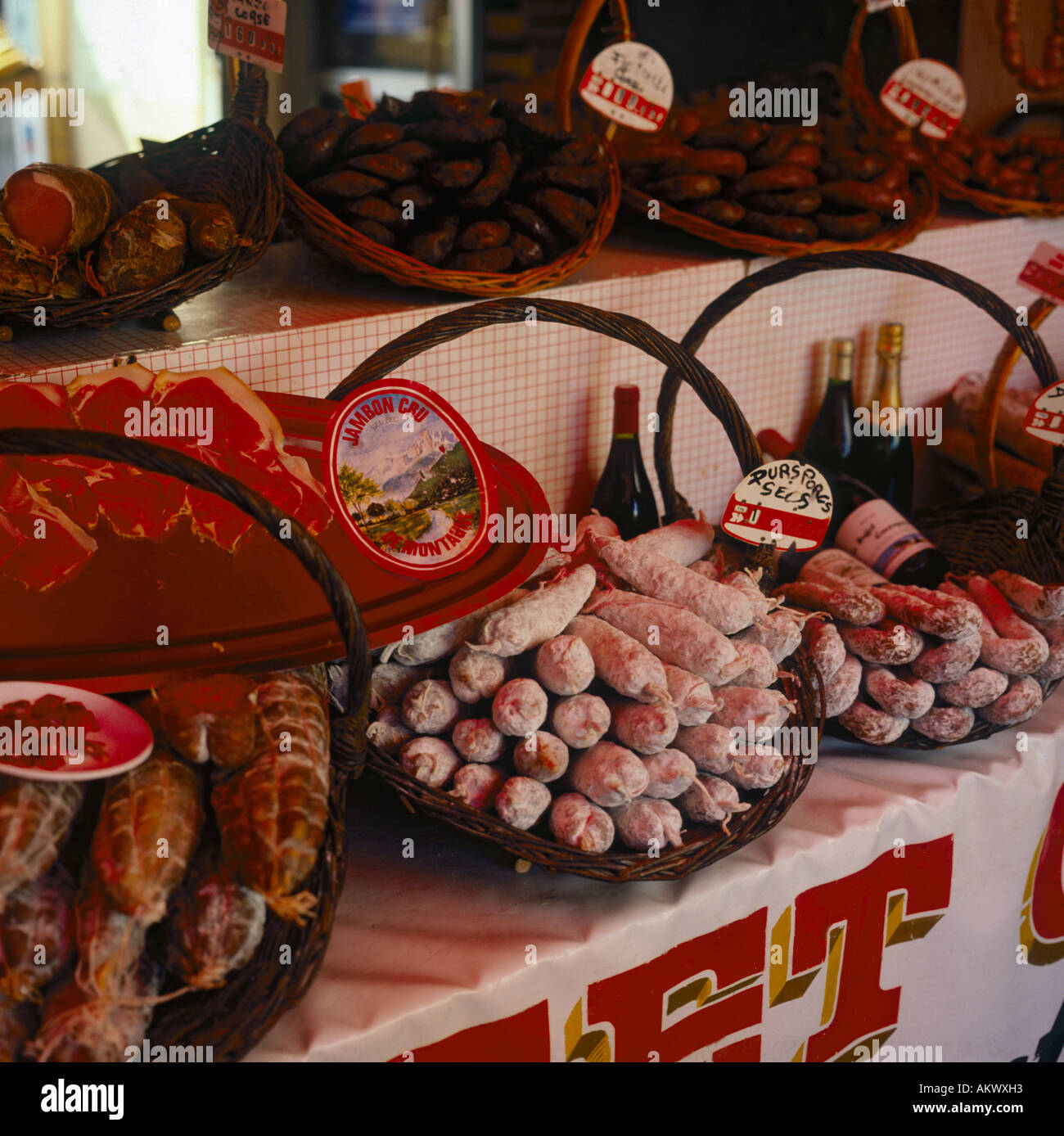 Colourful display of spicy meats and sausages in wicker baskets with bottles of wine on market stall in the South of France Stock Photo