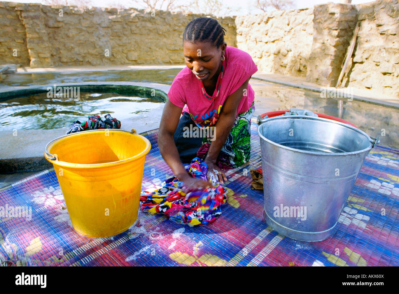 A Dogon woman washes clothes by hand at village well Stock Photo