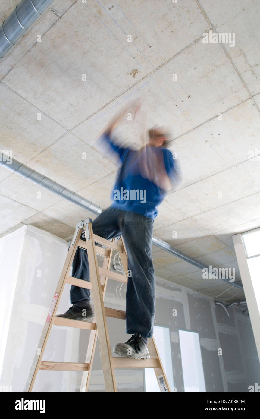 Construction worker on the ladder works at the ceiling Stock Photo