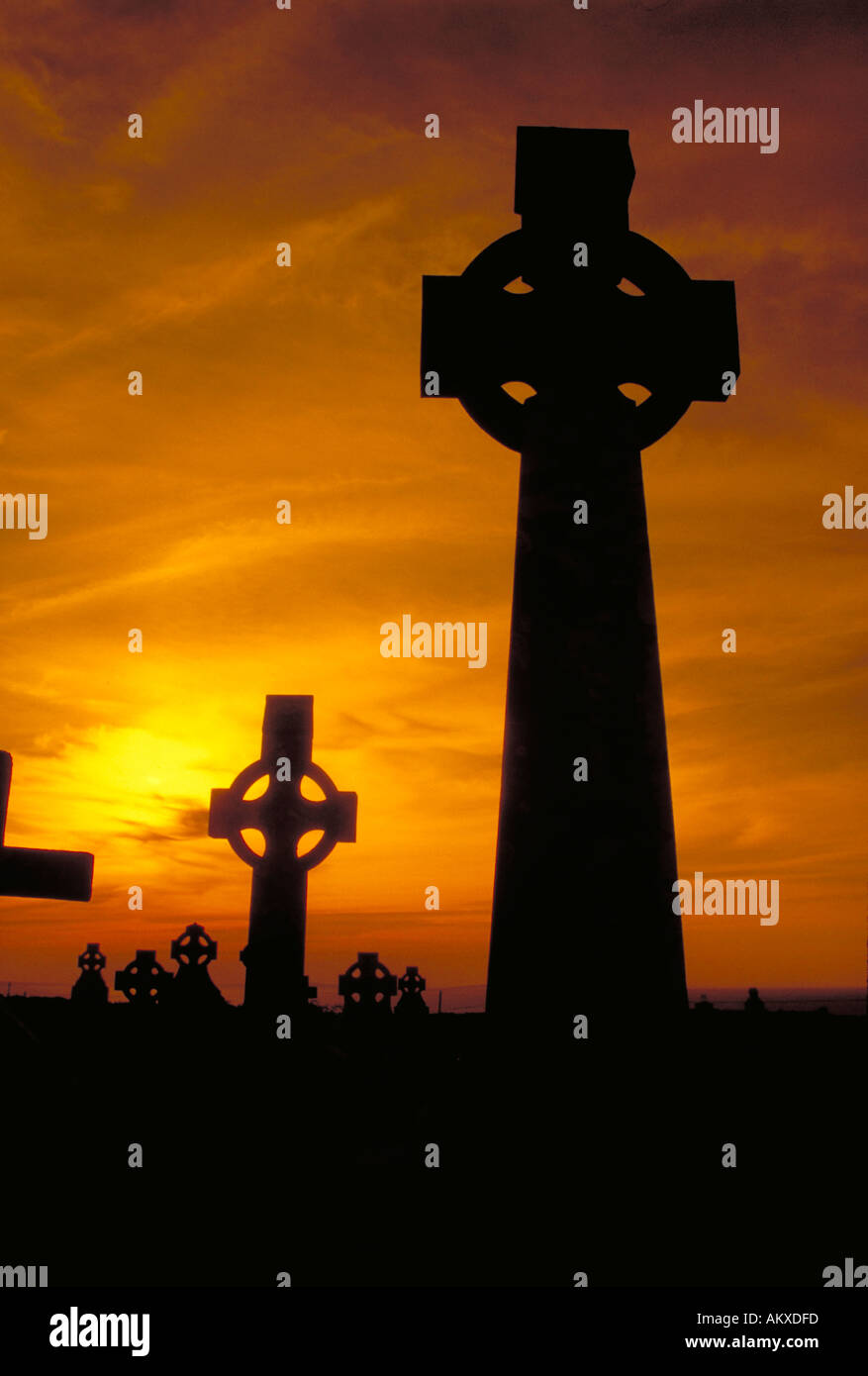 Two Celtic Crosses are silhouetted against golden sunset light in an Ancient Cemetery. County Clare, Ireland Stock Photo