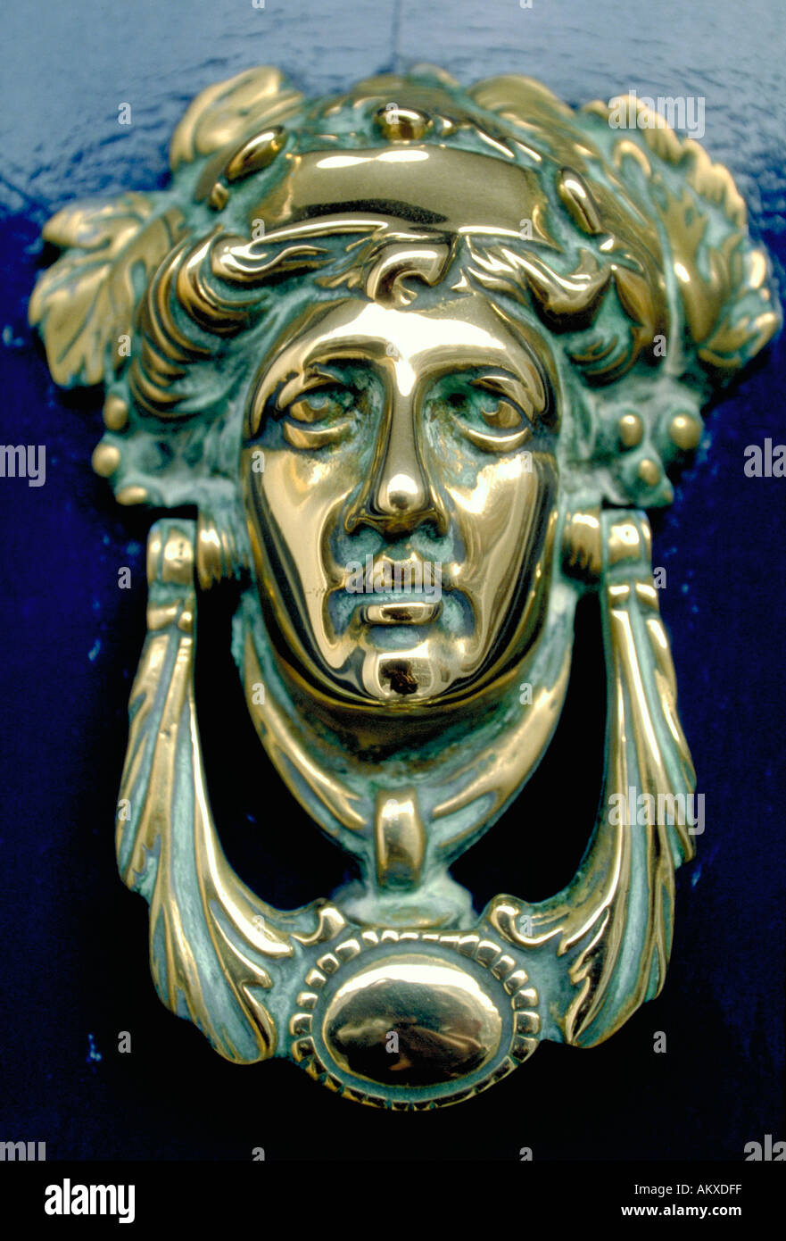 A brass door knocker in the shape of a woman s face with a laurel crown is mounted on a bright blue door Dublin Ireland Stock Photo