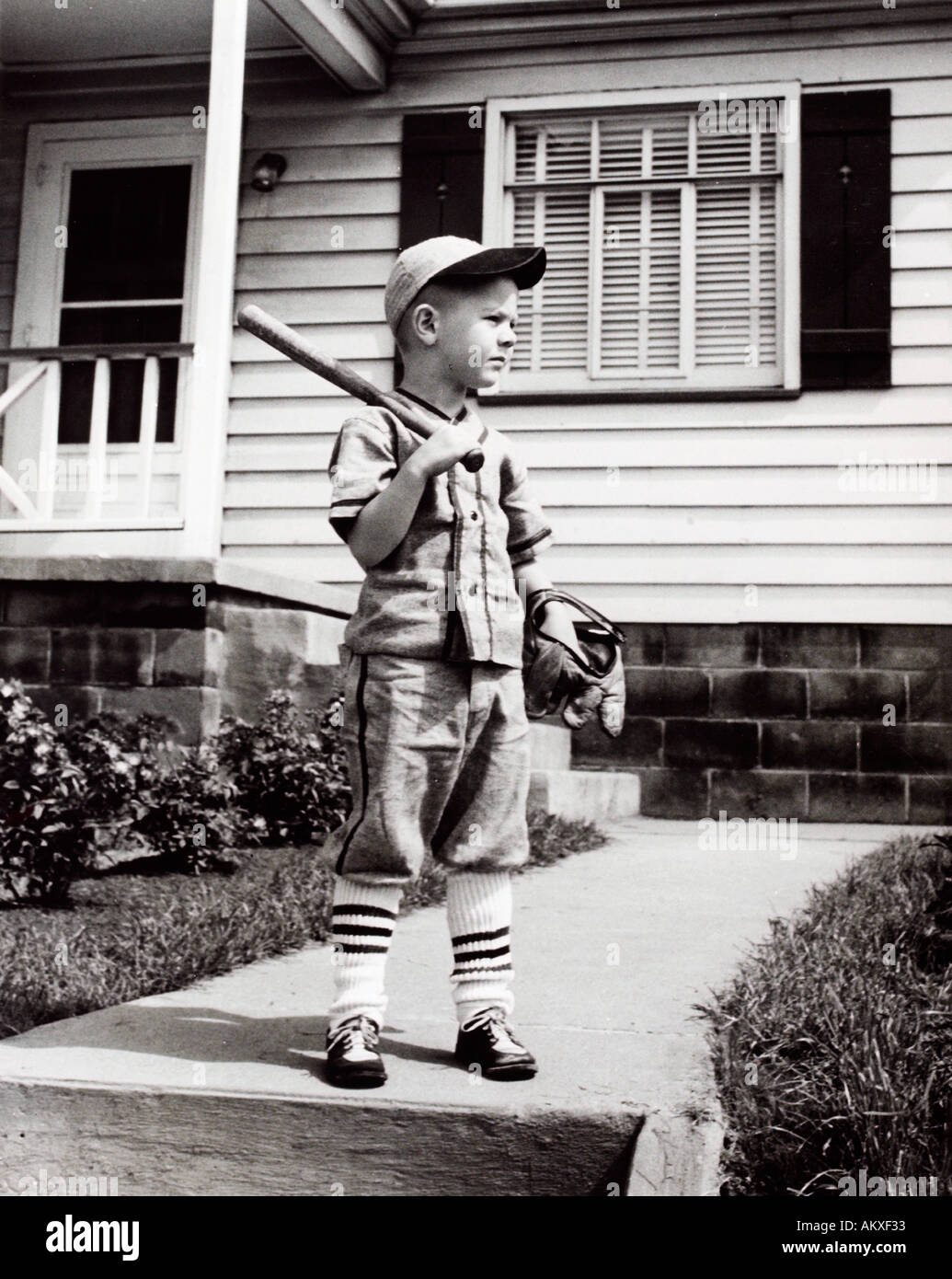 Young boy posing in baseball uniform with bat and glove in front of house in 1950 s Stock Photo