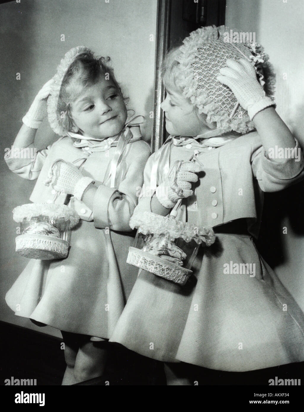 Cute little blond girl posing in mirror wearing fancy Easter outfit in 1950 s Stock Photo