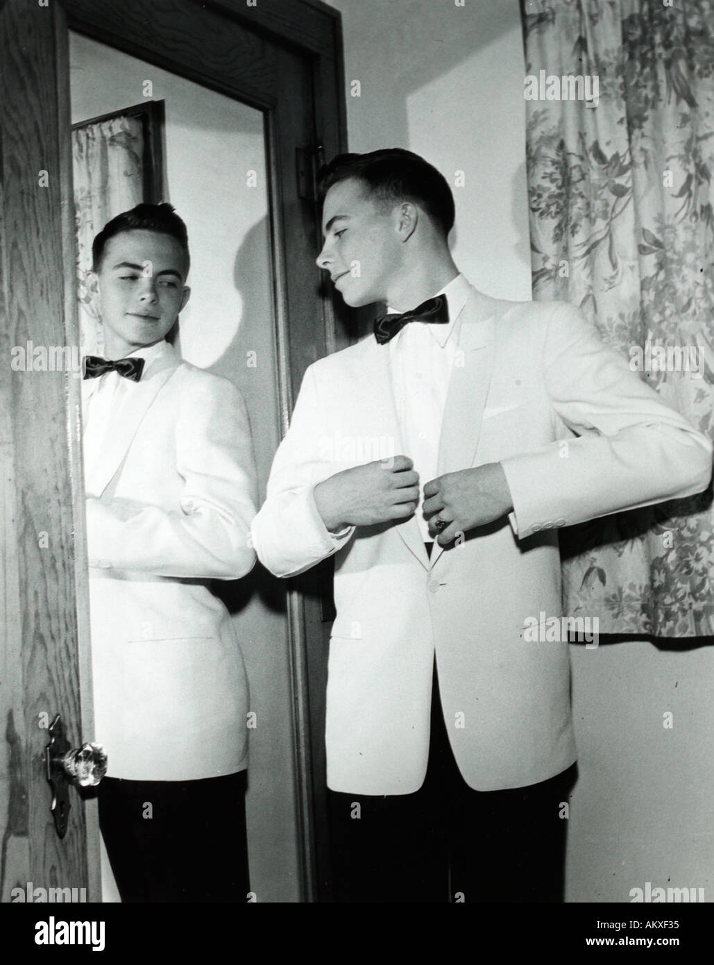 A teenage boy in a white tuxedo looking admiringly and confidently in mirror in 1950 s Stock Photo