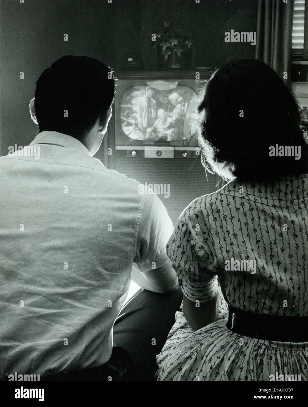 Two teenagers with backs toward camera watching vintage television in 1950 s Stock Photo
