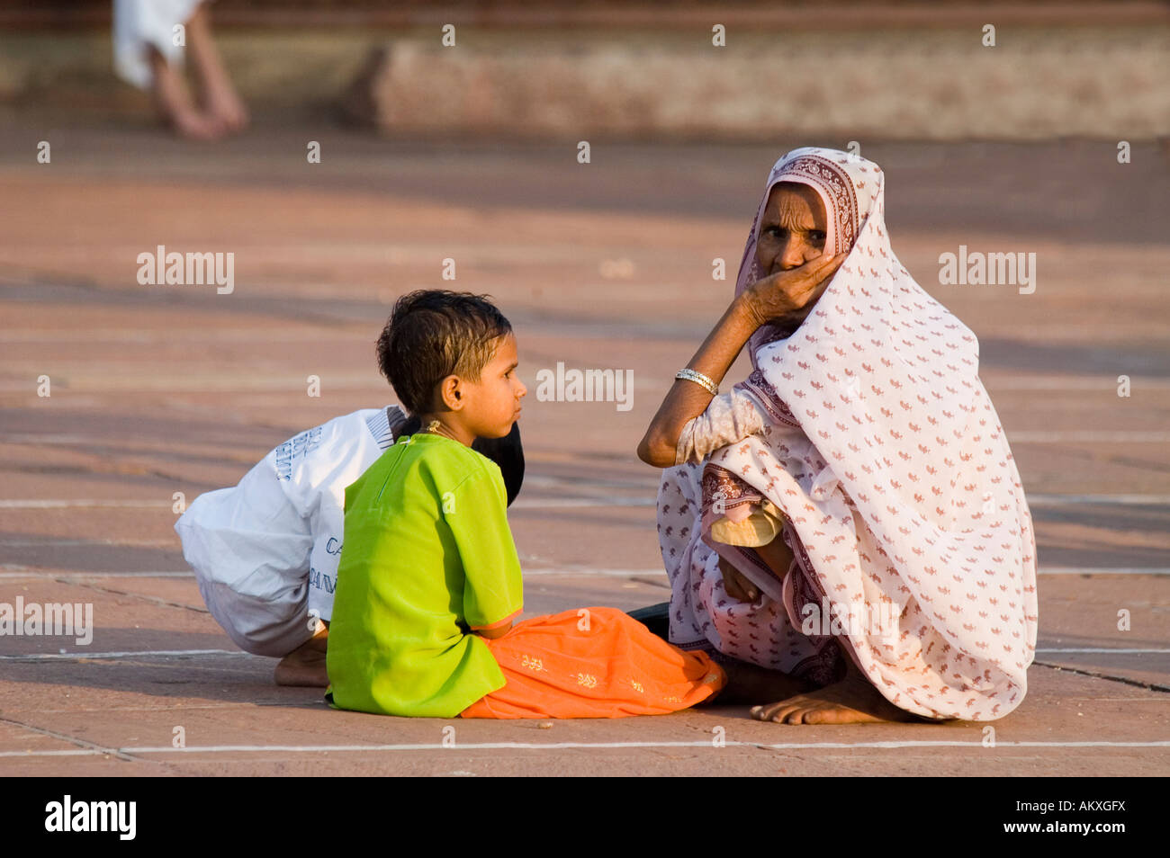 A Muslim grandmother sites with her grandsons in the massive courtyard of the Jama Masjid mosque in Old Delhi, India. - Stock Image