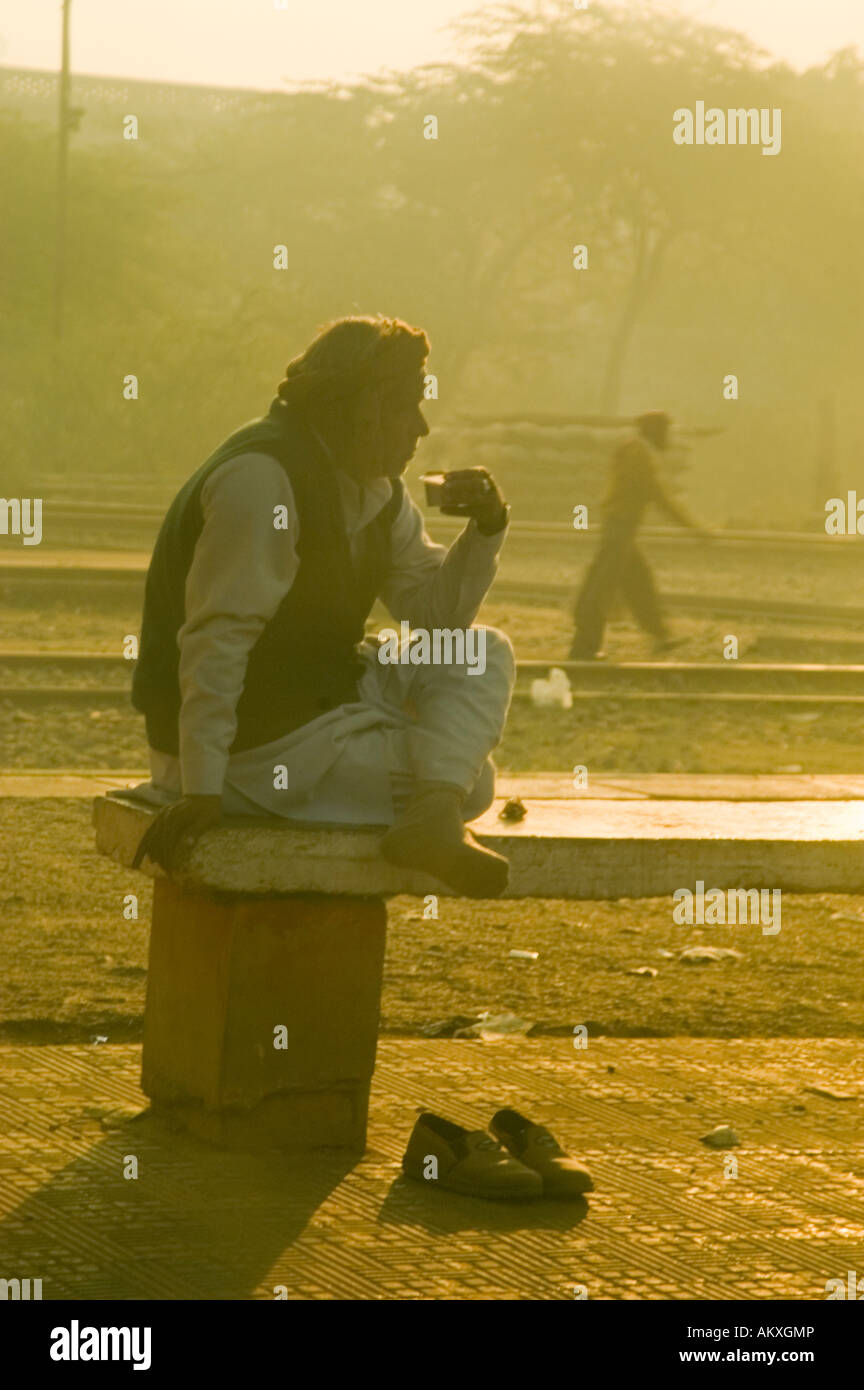 An Indian man sips his morning chai tea at a train station at sunrise on the outskirts of New Delhi, India. - Stock Image