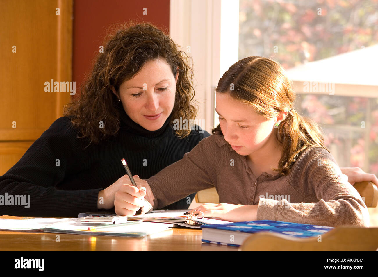 Mother helping her daughter with her home schooling homework in kitchen ...