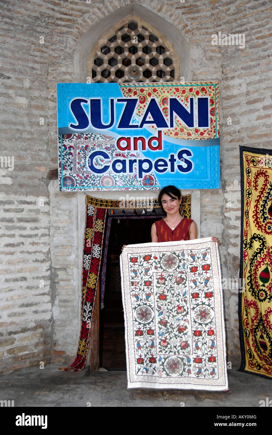 Young Uzbek salesgirl in front of her shop selling suzani and carpets in Madrasah Kukeldash Bukhara Uzbekistan Stock Photo
