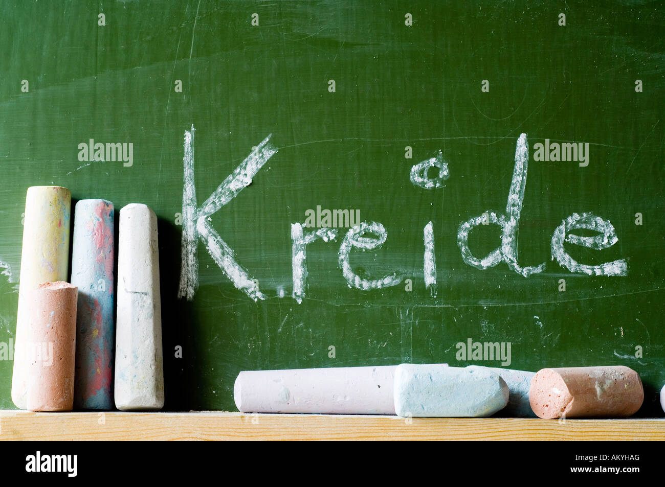 The word chalk is written on a chalkboard. In the foreground some pieces of coloured chalk. Stock Photo