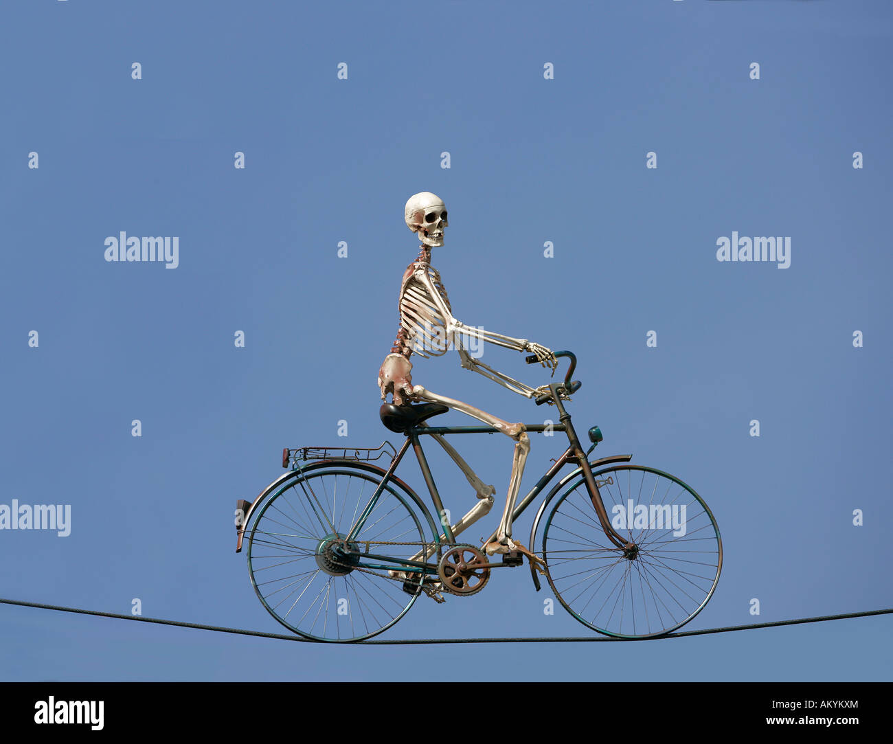 Skeleton riding a bike on a wire cable Stock Photo