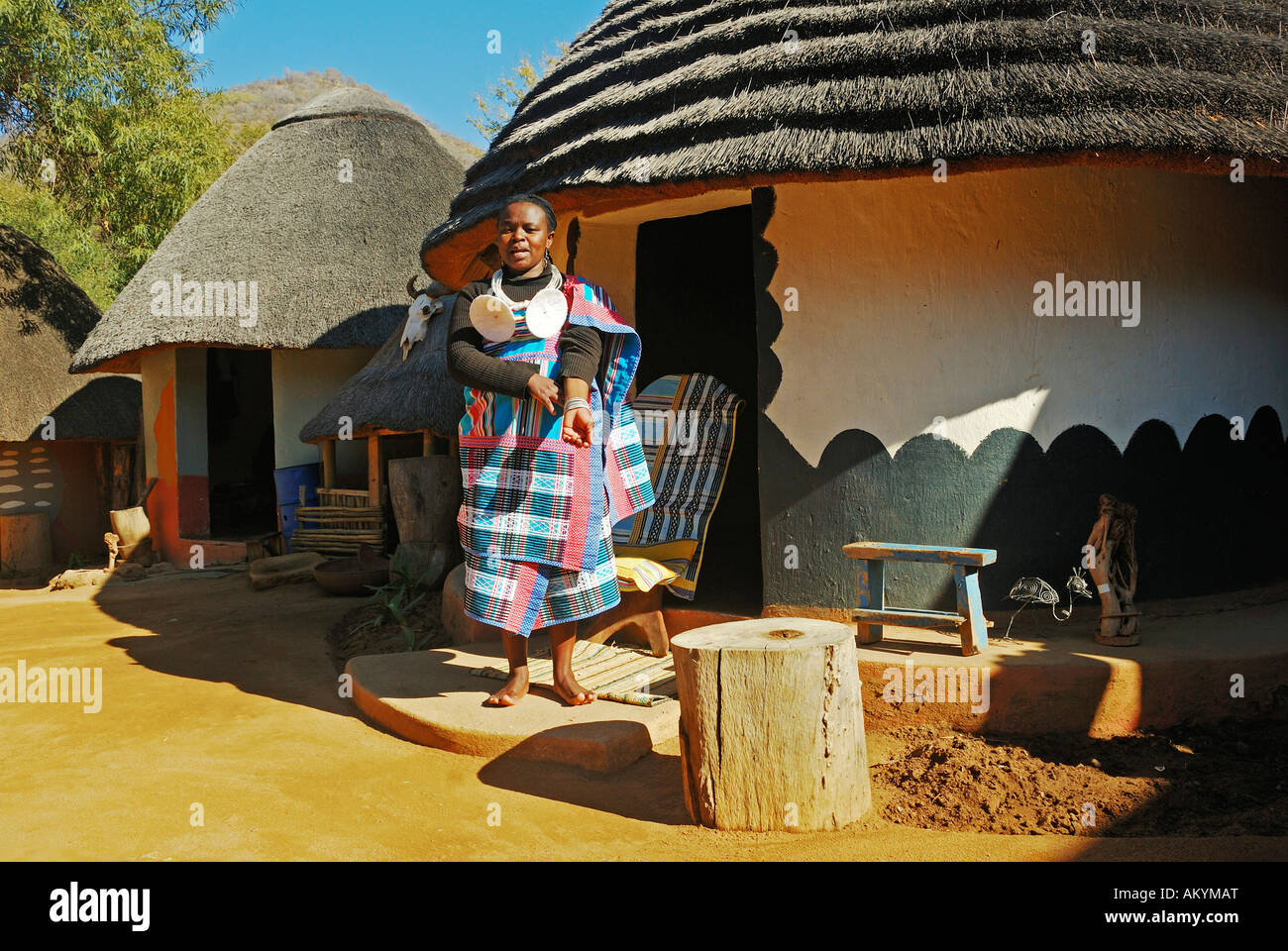 Dark skinned woman stands in front of a Ndebele hut and do houswork South Africa, Africa Stock Photo
