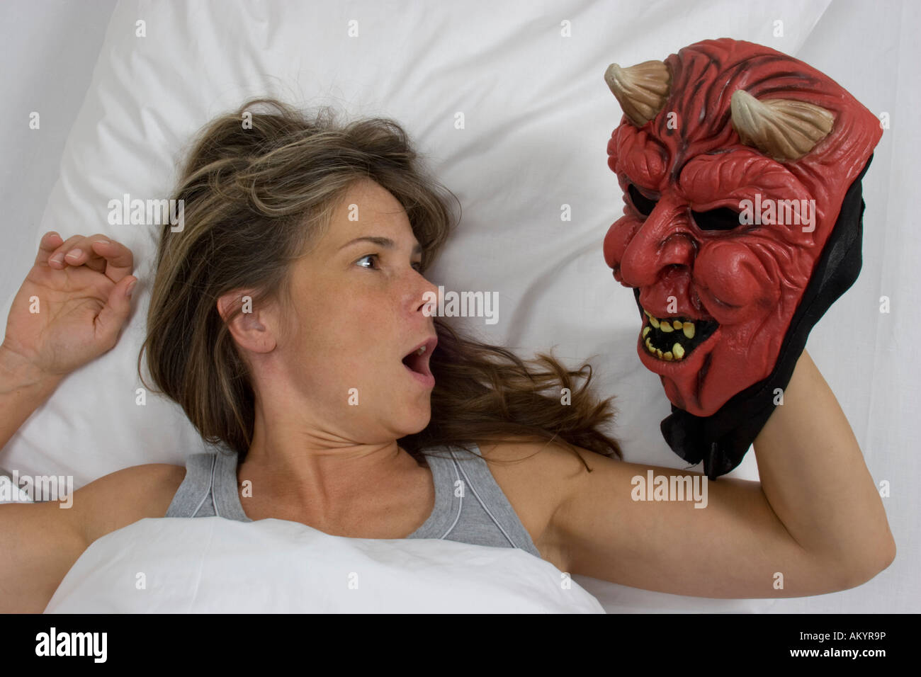 Woman lying in bed, devil mask Stock Photo