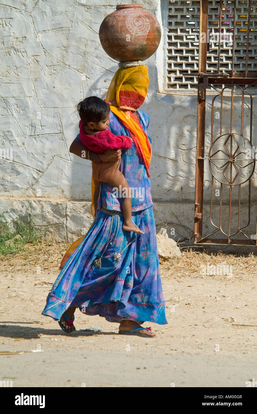 A Rajasthani Muslim woman with a burqua covering her face walks toward the village well with her young son on her - Stock Image