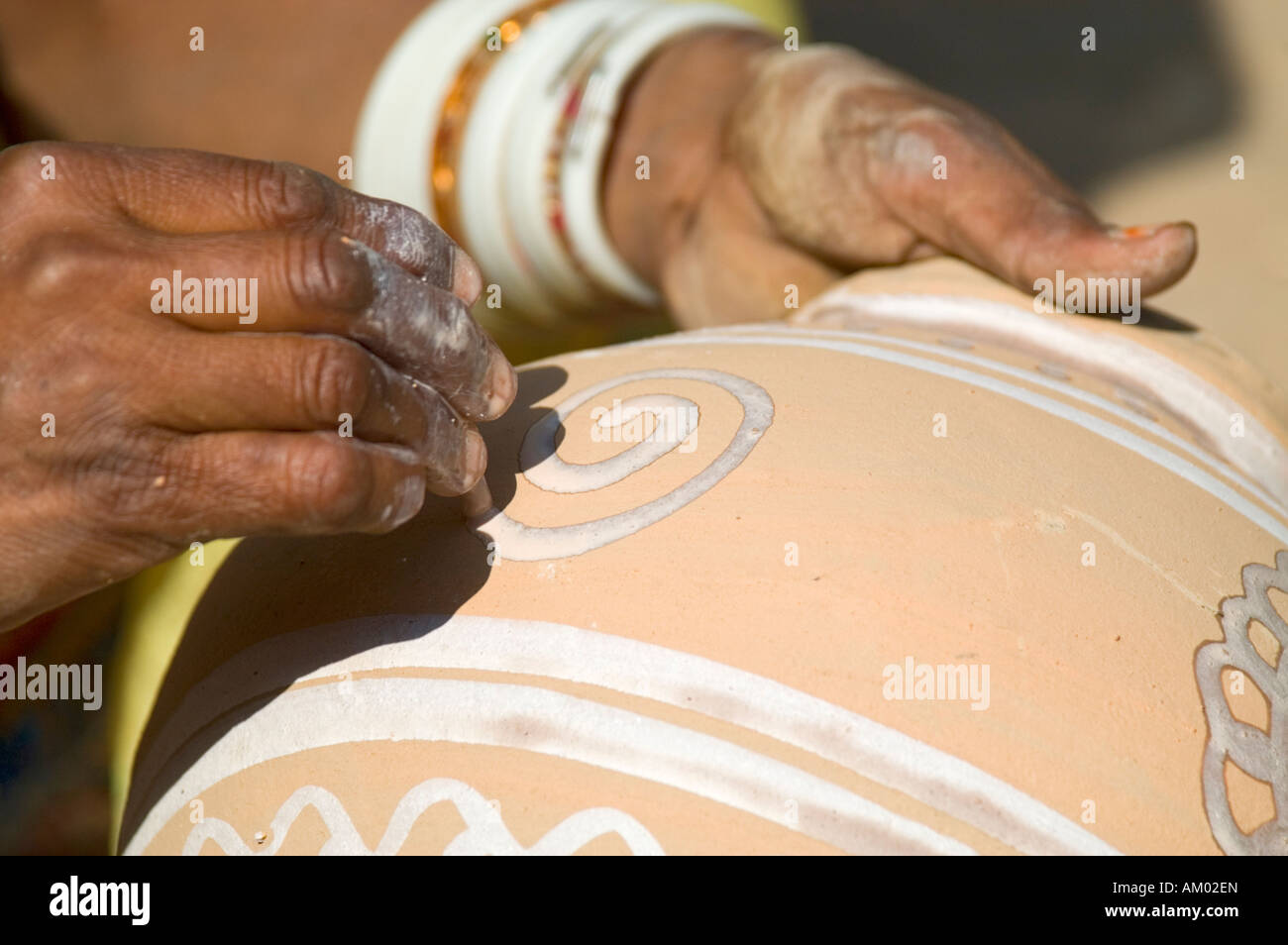 A Rajasthani woman paints the outside of a water pot her husband just made in the village of Nimaj, Rajasthan, India. - Stock Image