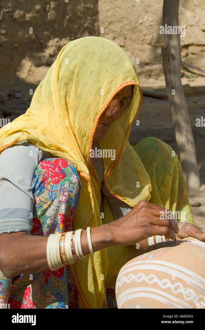 A Rajasthani woman paints the outside of a water pot her husband just made in the village of Nimaj, Rajasthan, India. - Stock Image