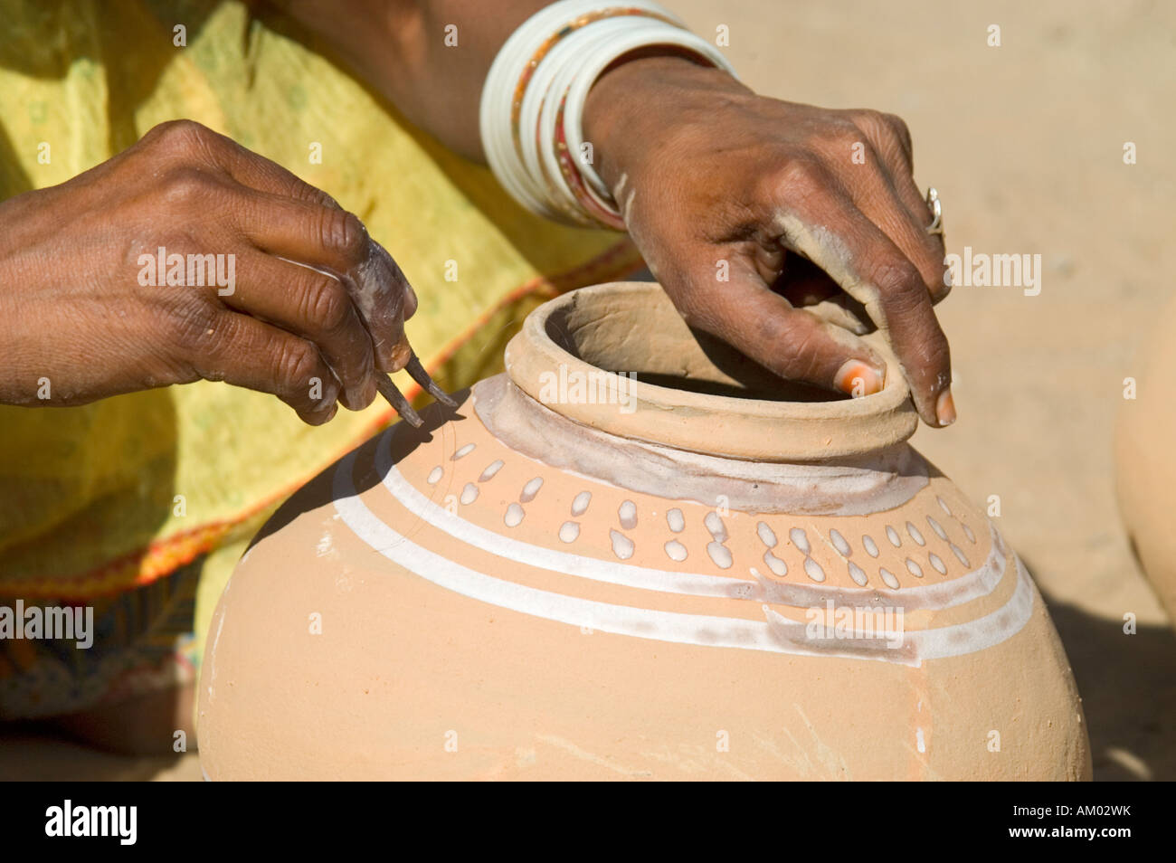 A Rajasthani woman paints the outside of a water pot her husband just made in the village of Nimaj, Rajasthan, India. - Stock Image
