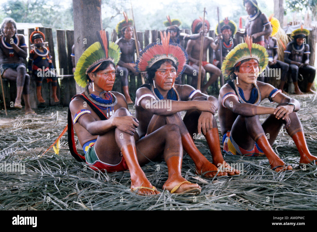 BRAZIL South America Amazon People Young Native Kayapo Indian men with painted bodies and feather headdresses sitting on ground Stock Photo