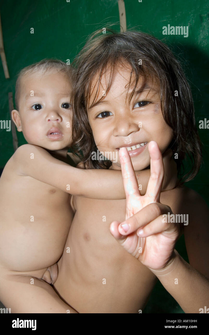 Girl holding her younger brother cheerily gives the victory salute, Phnom Penh, Cambodia Stock Photo