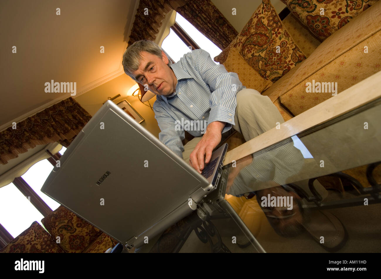 Middle aged man working on his laptop computer sitting on his sofa in the lounge of his house at home, UK Stock Photo