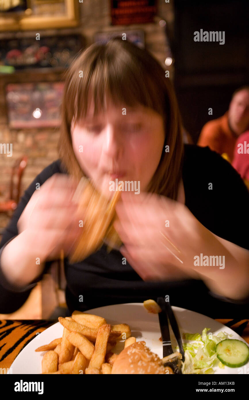 Young woman eating burger and chips in fast food restaurant Stock Photo