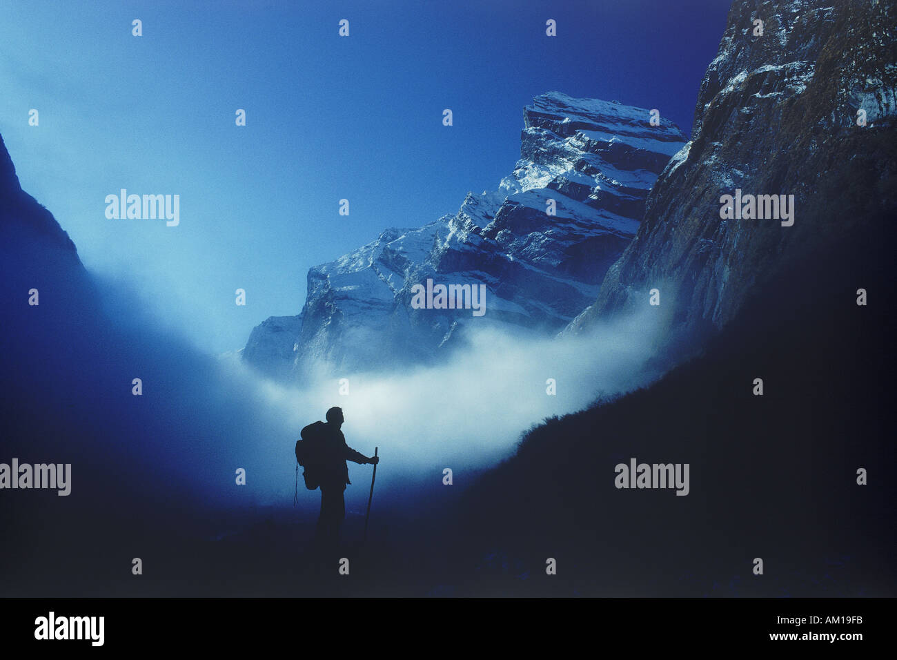 Lone trekker above clouds and below Himalayan peaks of Annapurnas in Nepal Stock Photo