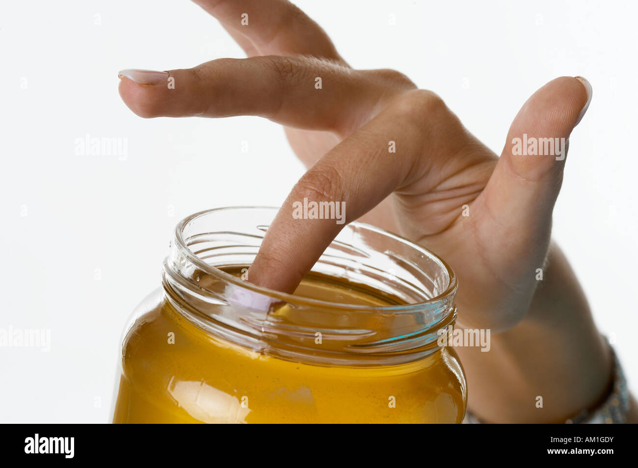 A finger is sticking in a glass full of honey Stock Photo