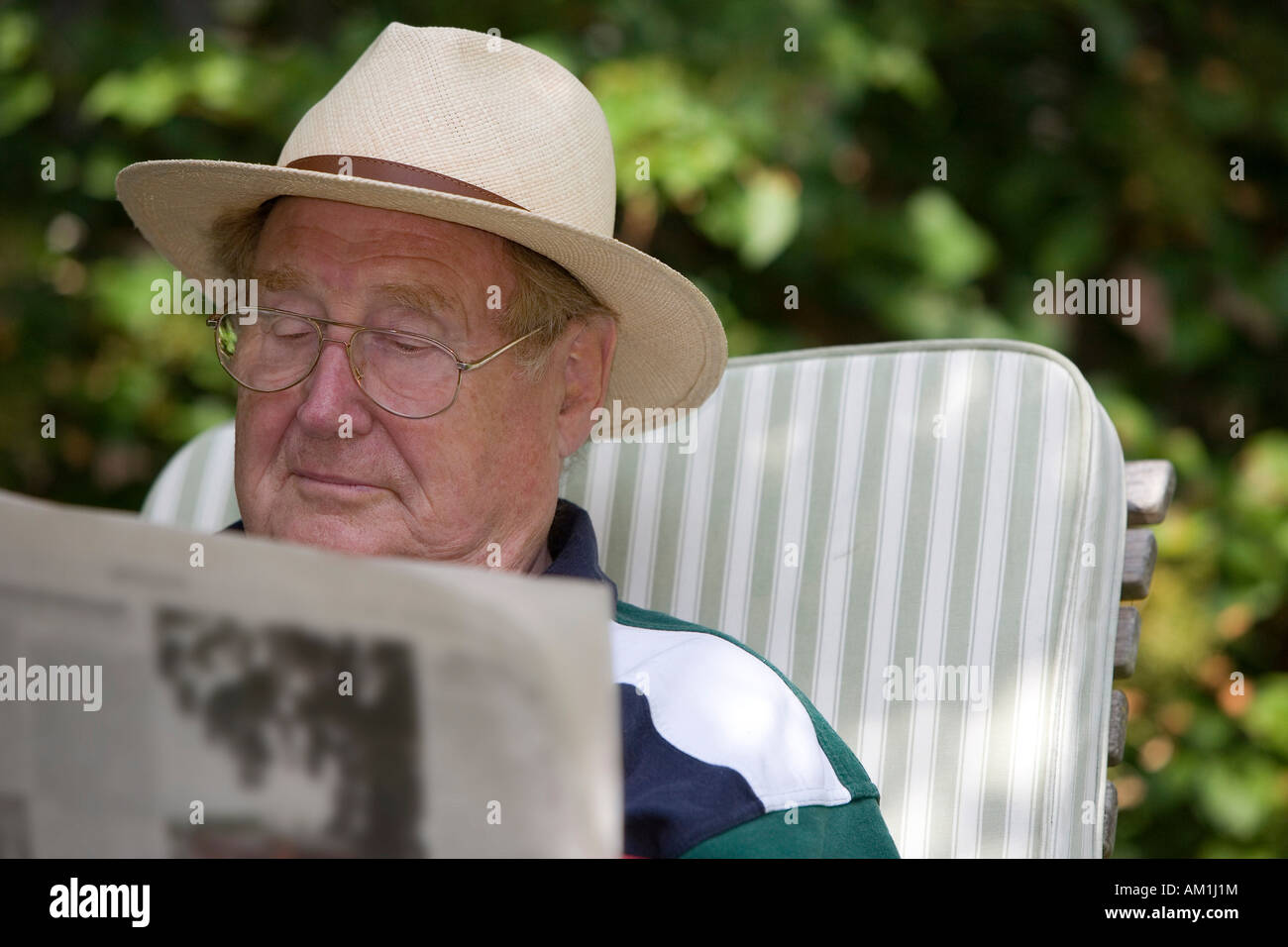 A relaxing senior citizen sitting in the garden reading a newspaper Stock Photo