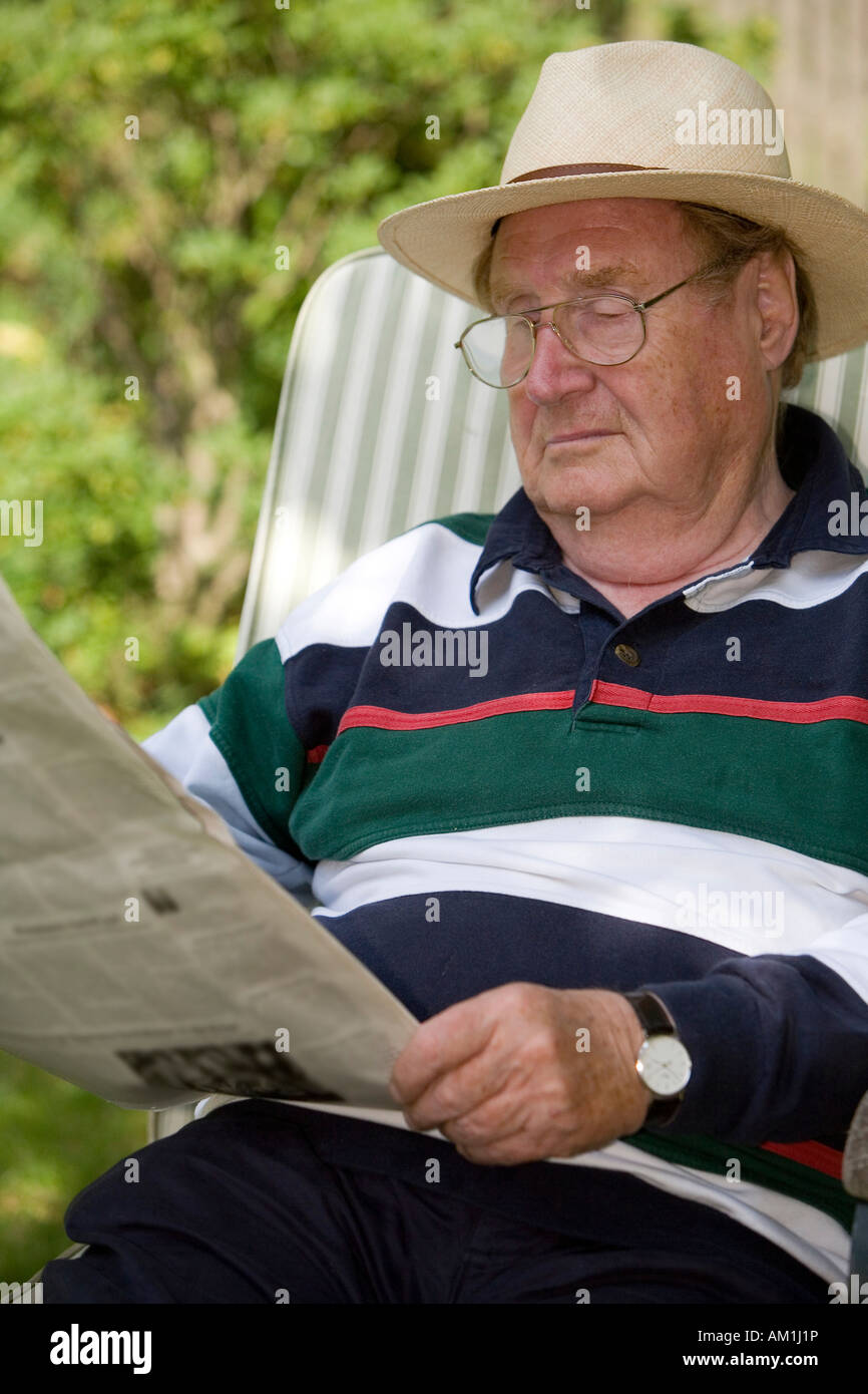 A relaxing senior citizen sitting in the garden reading a newspaper Stock Photo