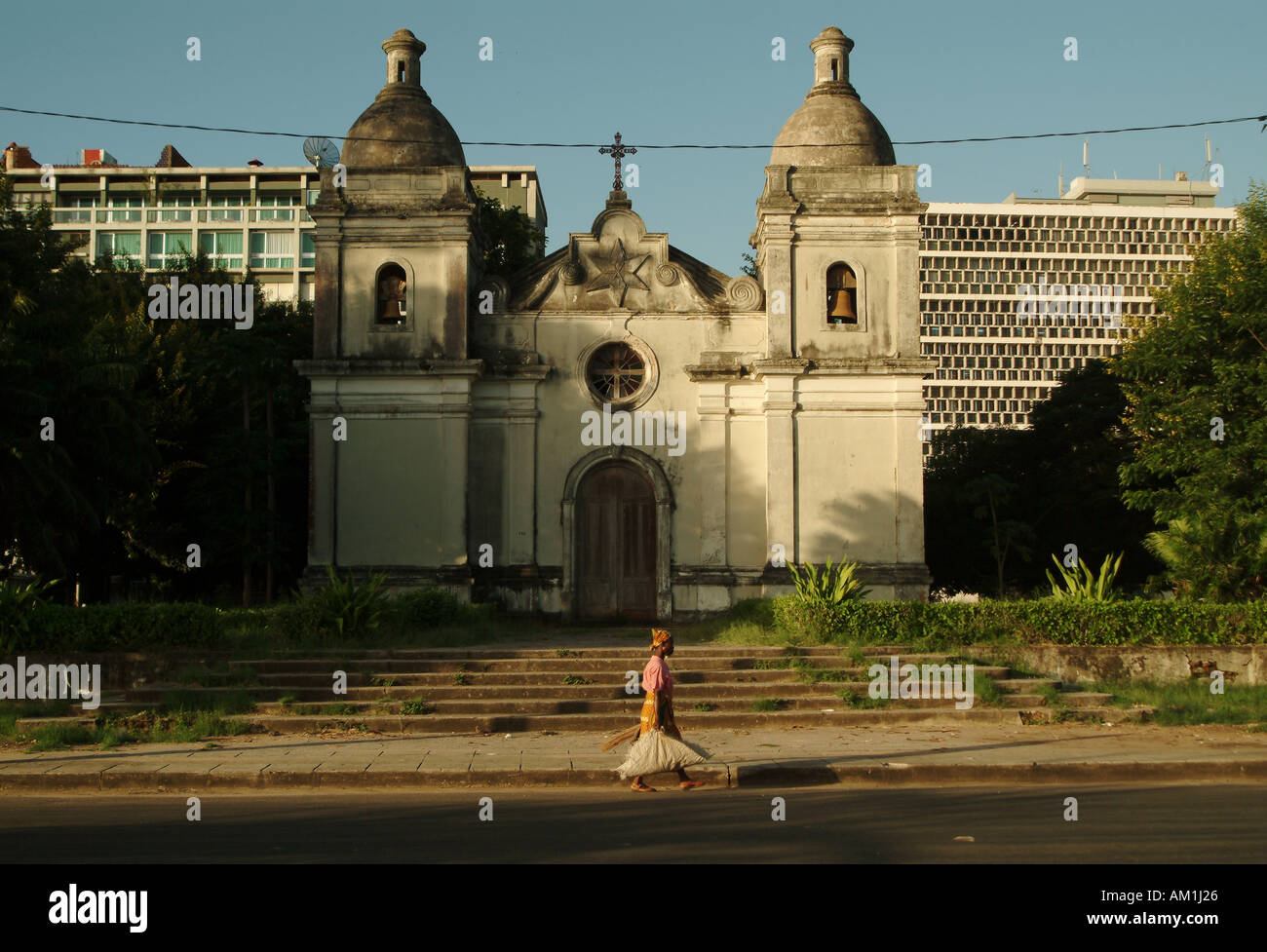 An African woman walks past an abandoned Portuguese cathedral in Quelimane city. Mozambique, Southern Africa Stock Photo