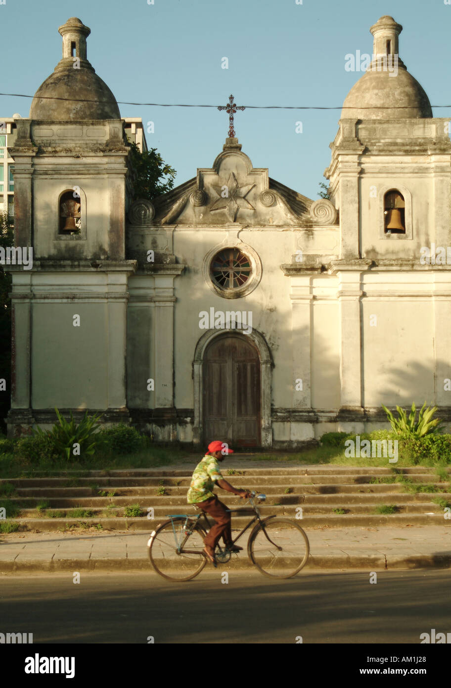 A man cycles his bike past an abandoned Portuguese cathedral in Quelimane city. Mozambique, Southern Africa Stock Photo