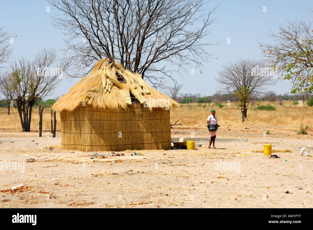 Local woman near a typical thatched-roof African round hut, Botswana Stock Photo