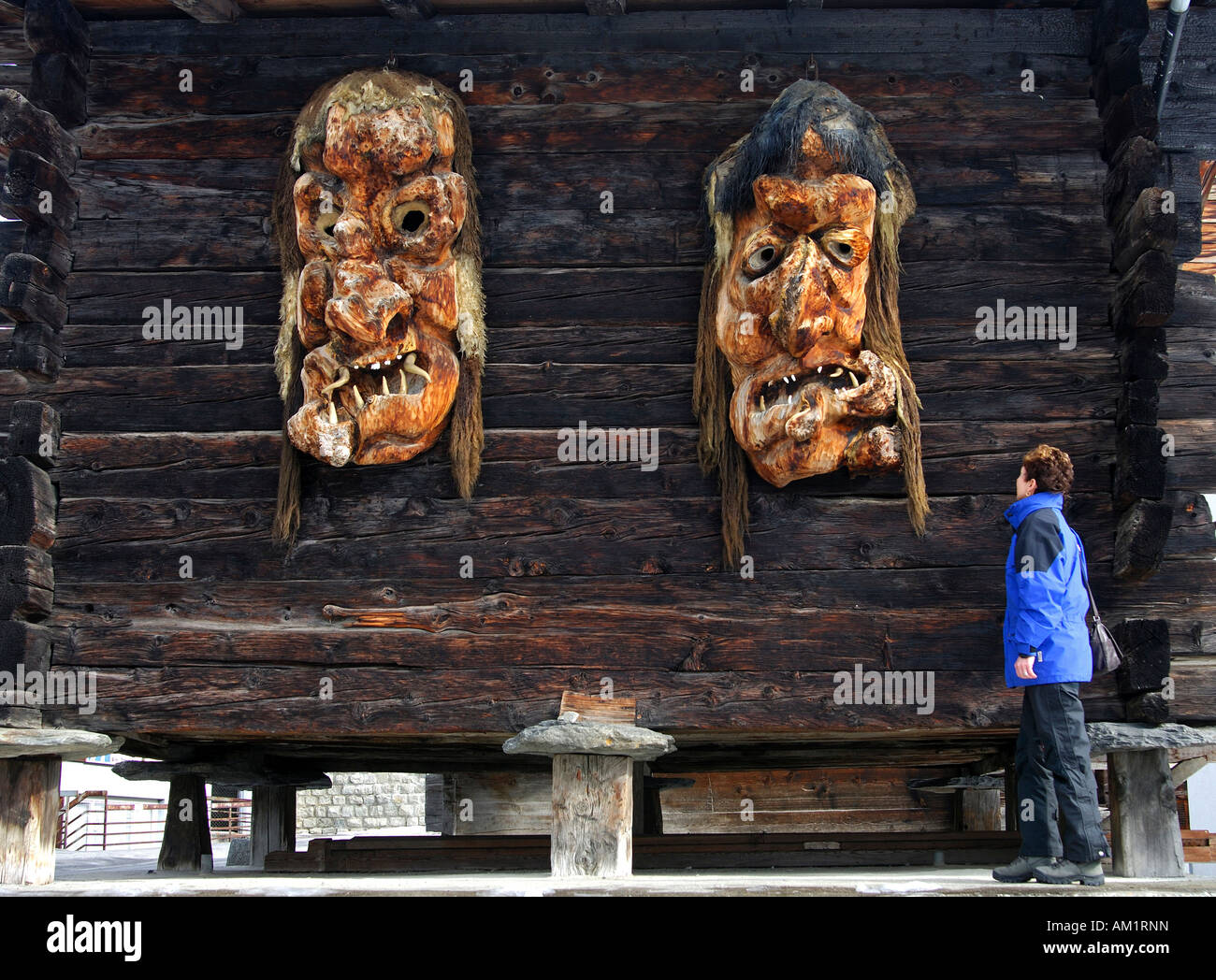 Women looks at a pair of oversized traditional wooden masks made of Swiss pine wood, Wiler, Loetschental, Valais, Switzerland Stock Photo